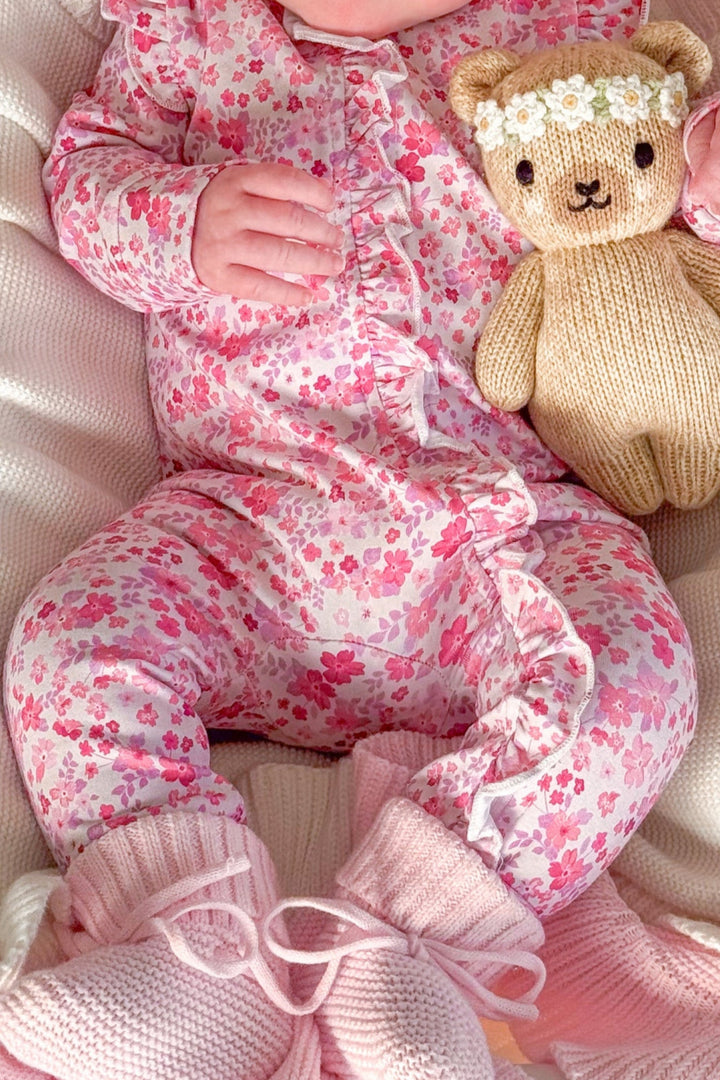 Baby in pink floral outfit with teddy bear on white blanket